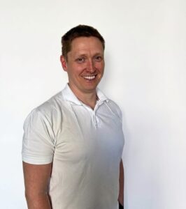 Kvinne smilende mann i hvit polo foran hvit bakgrunn.