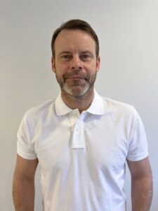 Mann med kort hår og skjorte foran en lys vegg.