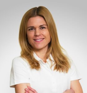 Kvinne i hvit uniform smilende mot kamera, helsepersonell, portrett.