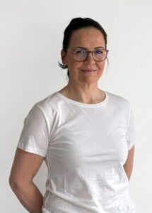 Kvinne med briller i hvit t-skjorte smilende mot kamera.
