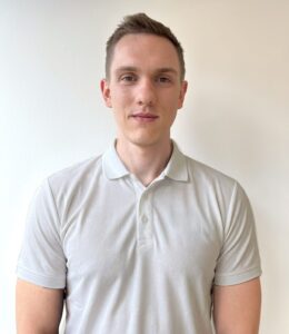 Kvinne i hvit polo-shirt foran lys vegg, smilende og rolig.
