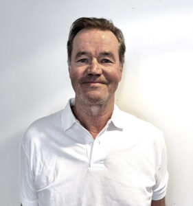 Jens Tingulstad, profesjonell helsepersonell med hvit skjorte, smilende foran en lys bakgrunn.