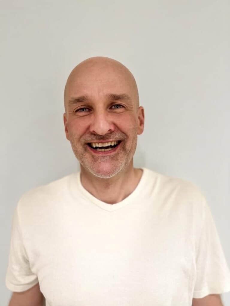 Smilende mann med hvit t-skjorte mot lys bakgrunn.