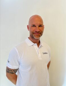 Kiropraktor fra Limbra smilende med hvit polo, bakgrunn i lyse farger.