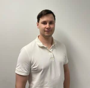 Mann i hvit polo-shirt står mot en lys vegg.