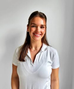 Smilende kvinne i hvit polo-shirt mot lys bakgrunn.