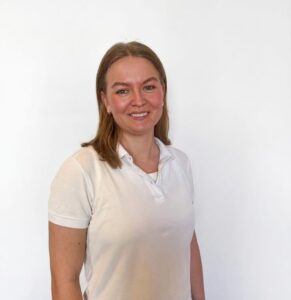 Kvinne smilende terapeut i hvit skjorte mot hvit bakgrunn.