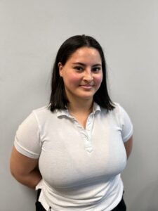 Kvinne smilende med mørkt hår i hvit polo foran nøytral vegg.