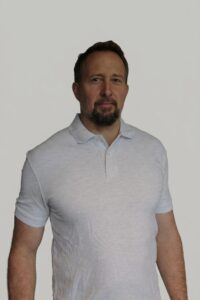 Mann i lys grå polo-shirt ser direkte mot kamera mot en hvit bakgrunn.