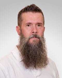 Mann med fullt skjegg og kort hår, portrett mot lys grå bakgrunn.