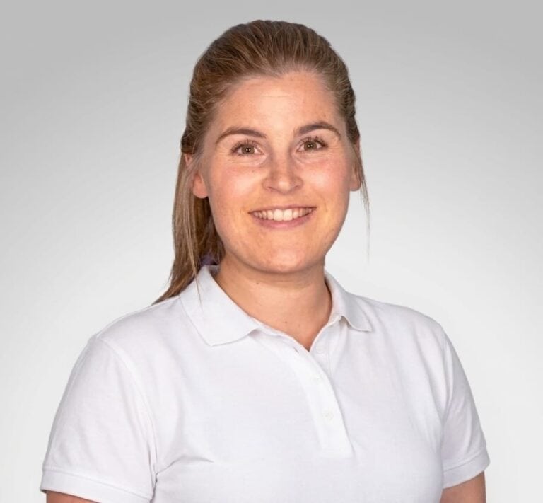 Kvinne smilende helsepersonell i hvit skjorte mot lys bakgrunn.