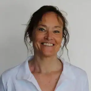 Kvinne med brunt hår og hvit skjorte smiler mot kamera.