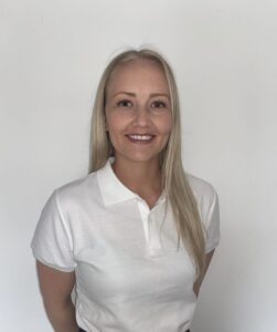 Smilende kvinne i hvit polo-shirt foran hvit vegg.