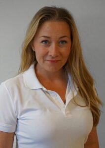 Kvinne i hvit polo smilende mot kamera, portrett.