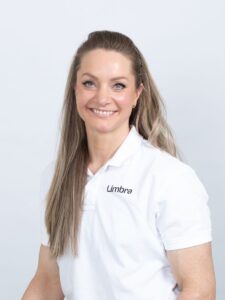 Lone Gilje, kiropraktor ved Limbra, smilende og kledd i hvitt, foran en lys bakgrunn.