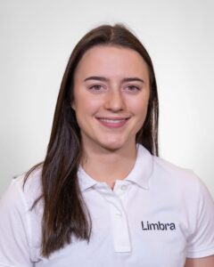 Kvinne i Limbra-uniform smiler mot kamera, hvit bakgrunn.