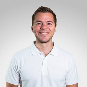 Marcus Ogre smilende mann i hvit polo mot lys grå bakgrunn.