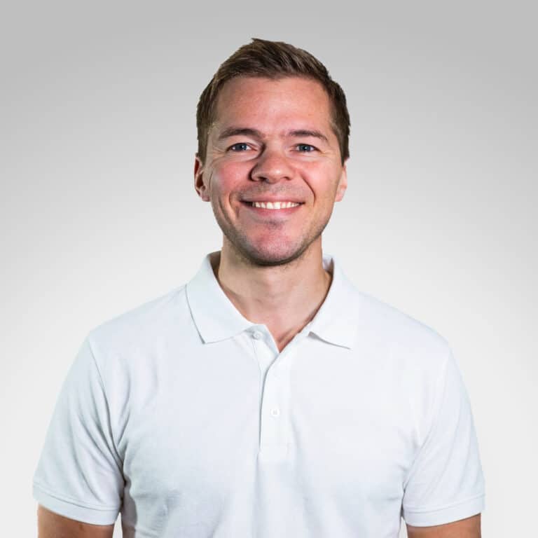 Marcus Ogre smilende mann i hvit polo mot lys grå bakgrunn.