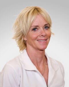 Kvinne i hvit skjorte smiler mot kamera, portrett.