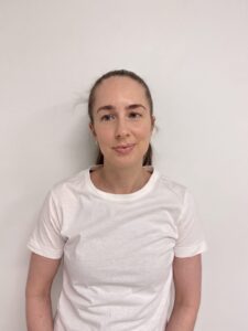 Kvinne med hvit t-skjorte mot hvit vegg, ser rolig ut.