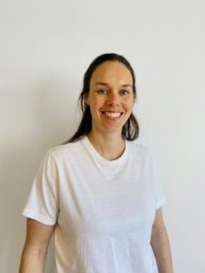 Kvinne smilende i hvit t-skjorte mot enkel hvit vegg.