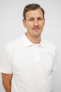 Kvinne i hvit polo-shirt smilende foran hvit bakgrunn, profesjonell portrett.