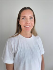 Smilende kvinne i hvit t-skjorte mot lys grå bakgrunn.