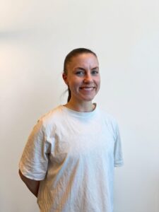 Smilende kvinne i hvit t-skjorte mot lys bakgrunn.