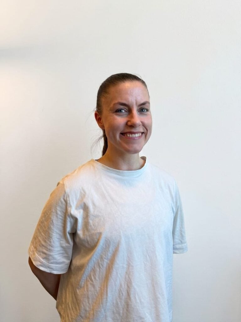 Smilende kvinne i hvit t-skjorte mot lys bakgrunn.