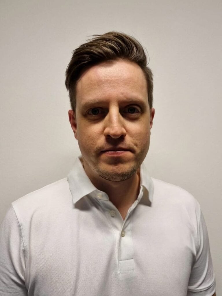 Mann i hvit skjorte ser direkte inn i kamera mot en lys bakgrunn.