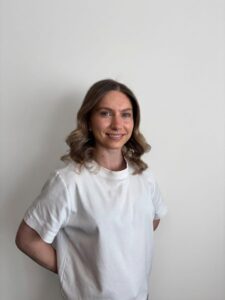 Kvinne smiler foran hvit vegg, portrett, helse og velvære.