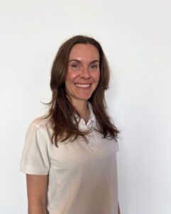 Kvinne smilende i hvit t-skjorte mot hvit bakgrunn.