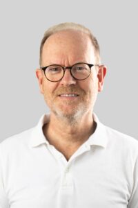 Øistein Haagensen, kiropraktor med lang erfaring, smilende foran en lys grå bakgrunn.