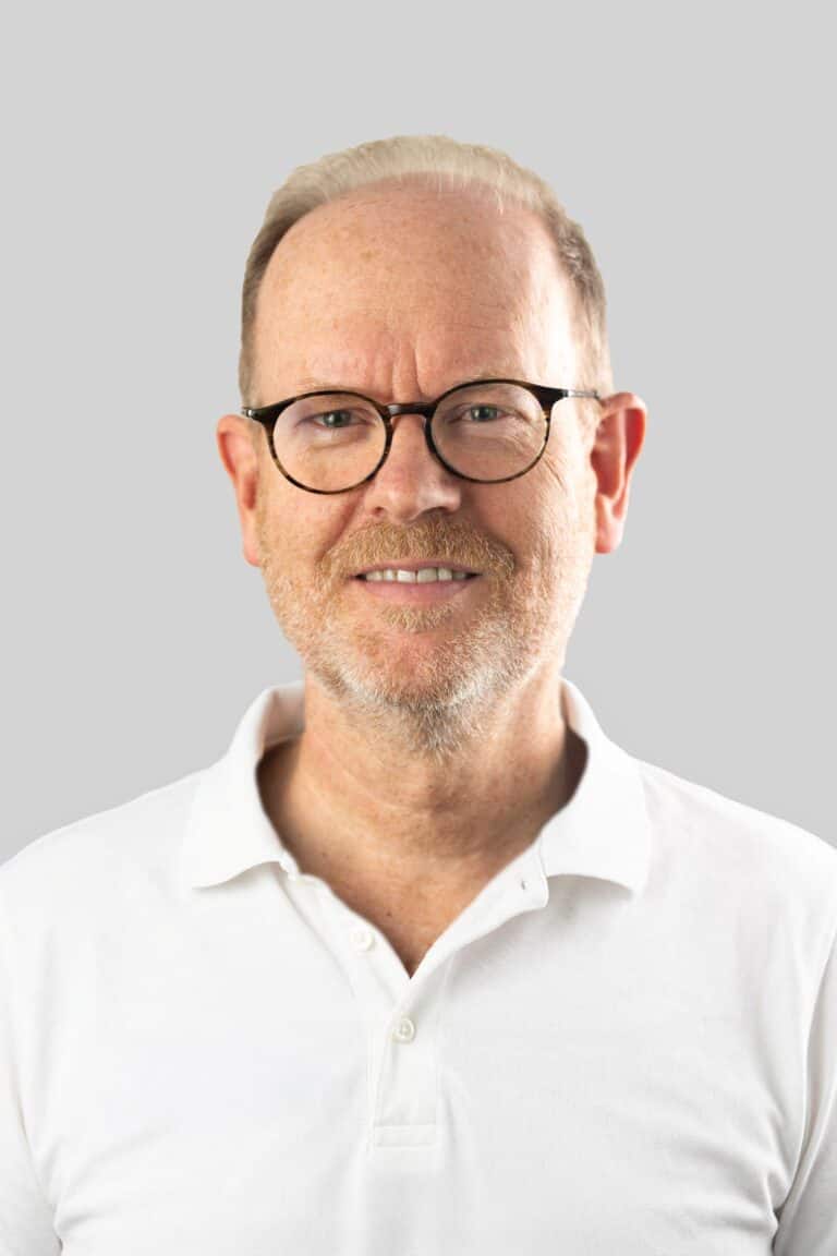 Øistein Haagensen, kiropraktor med lang erfaring, smilende foran en lys grå bakgrunn.