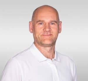 Kiropraktor med hvit skjorte smilende mot kamera.