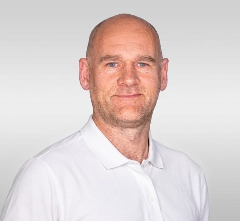 Kiropraktor med hvit skjorte smilende mot kamera.