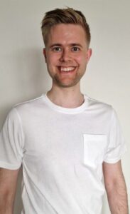 Ung mann smiler, portrett, hvit t-skjorte, innendørs.