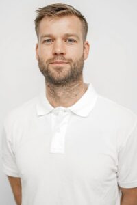 Mann med lyst hår og skjegg i hvit polo, portrett.