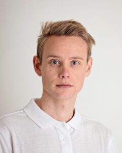 Ung mann med blond hår og hvit polo shirt mot en lys bakgrunn.