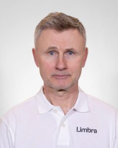 Kiropraktør med Limbra-logo på hvit skjorte, nærbilde av ansikt, nøytral bakgrunn.