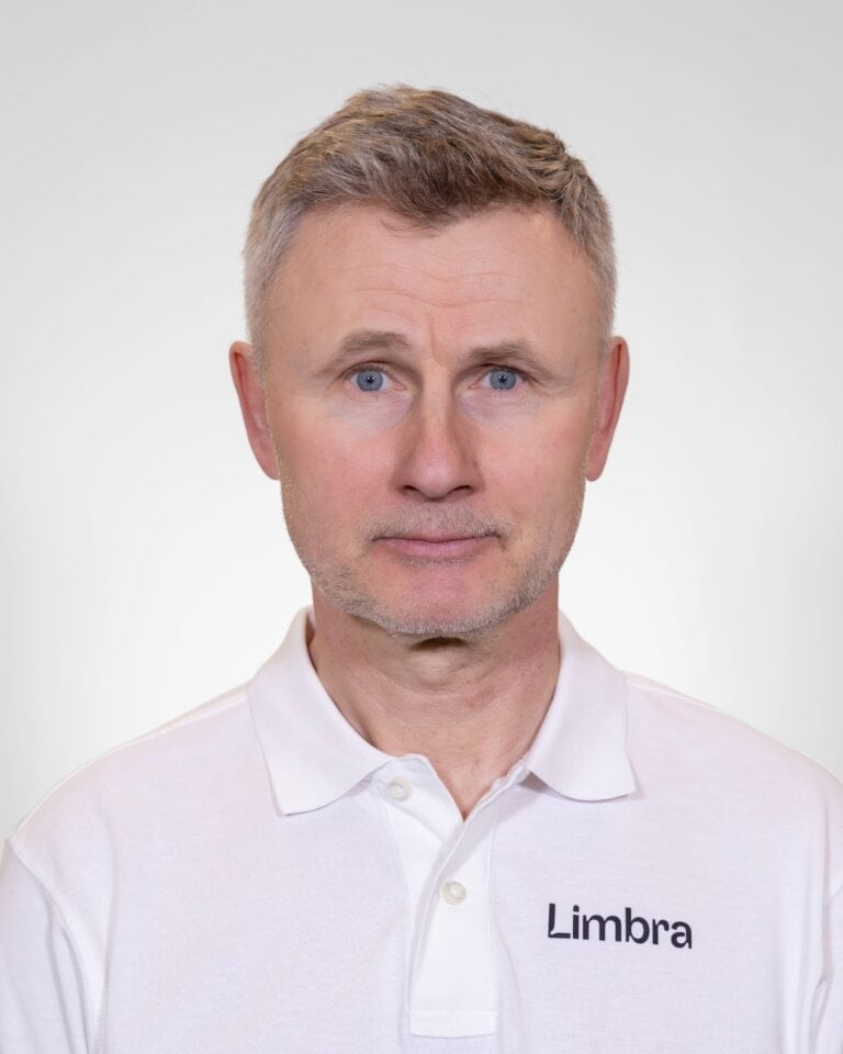 Kiropraktør med Limbra-logo på hvit skjorte, nærbilde av ansikt, nøytral bakgrunn.
