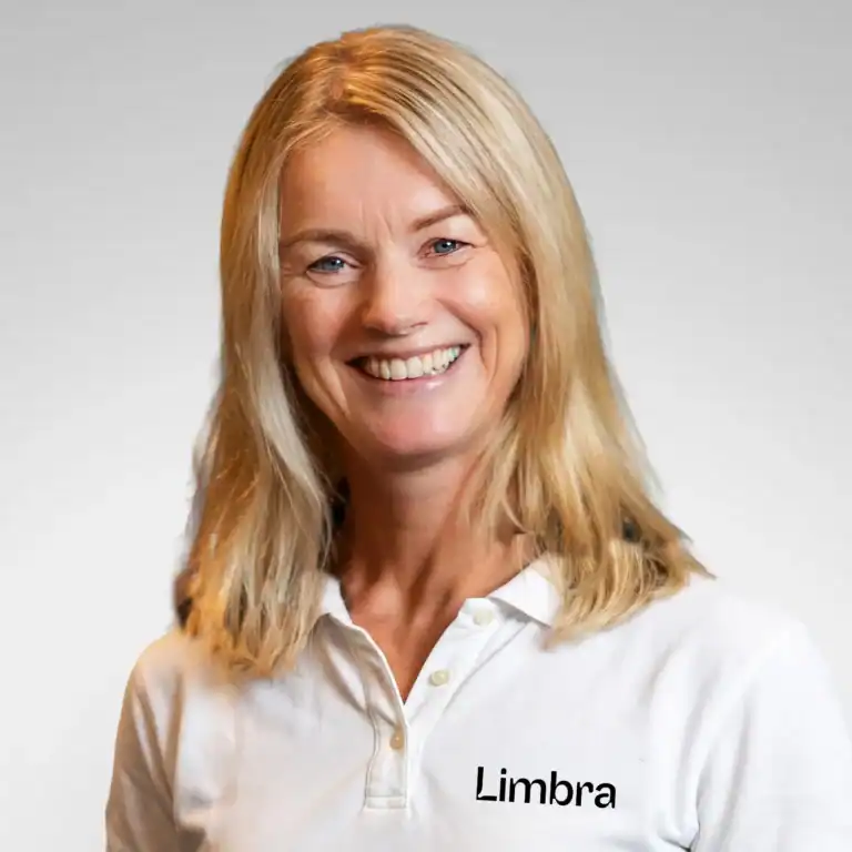 Kvinne med blondt hår smiler mot kamera, iført hvit Limba-rutete skjorte.