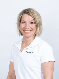 Kvinne i hvit Limbraklær smiler mot kamera, portrett.