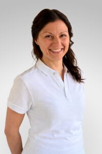 Kvinne smilende i hvit skjorte mot lys grå bakgrunn.
