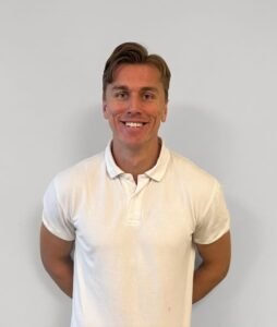 Kvinne smiler i hvit polo foran hvit vegg.