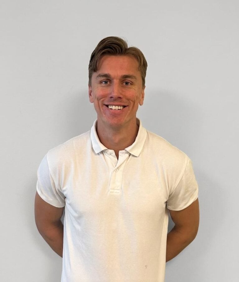 Kvinne smiler i hvit polo foran hvit vegg.