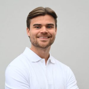 Ung mann med hvit skjorte smilende mot kamera.