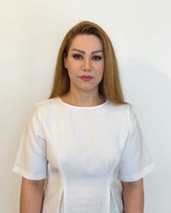 Kvinne med lang, blond hår og hvit topp ser direkte inn i kameraet.