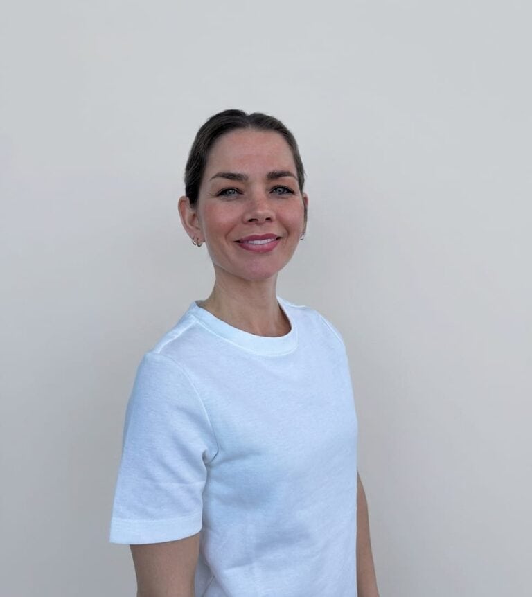 Kvinne smilende kvinne i hvit t-skjorte mot lys bakgrunn.