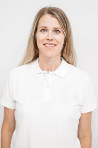 Kvinne med blondt hår i hvit polo smilende mot kamera.